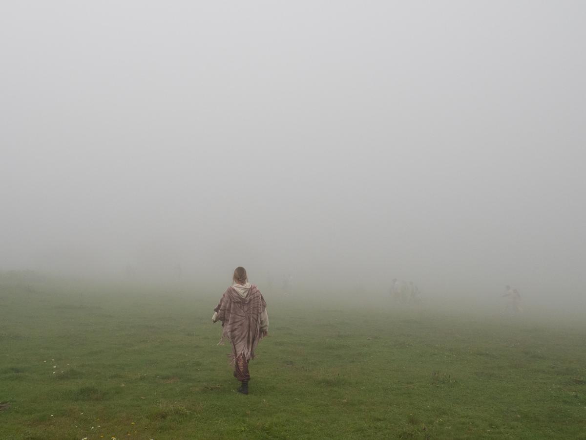 Leyla walking away across a green field into thick fog