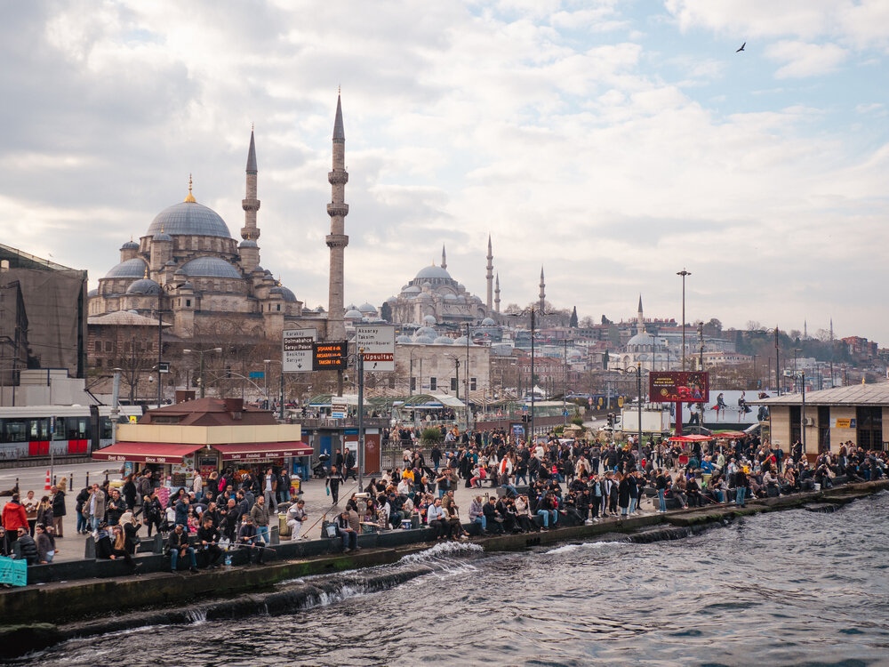 The Eminönü waterfront in Istanbul, people crowded along the water with the New Mosque and its minarets behind