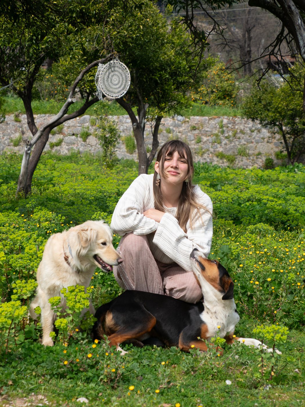 Leyla Fıratlı sitting in a flowering garden with two dogs