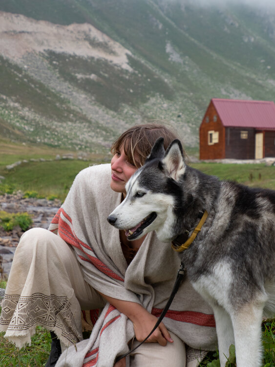 Leyla wrapped in a blanket, hugging a husky in a mountain meadow